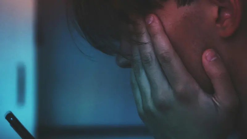 Una persona con lo smartphone in mano e il volto tra le mani
