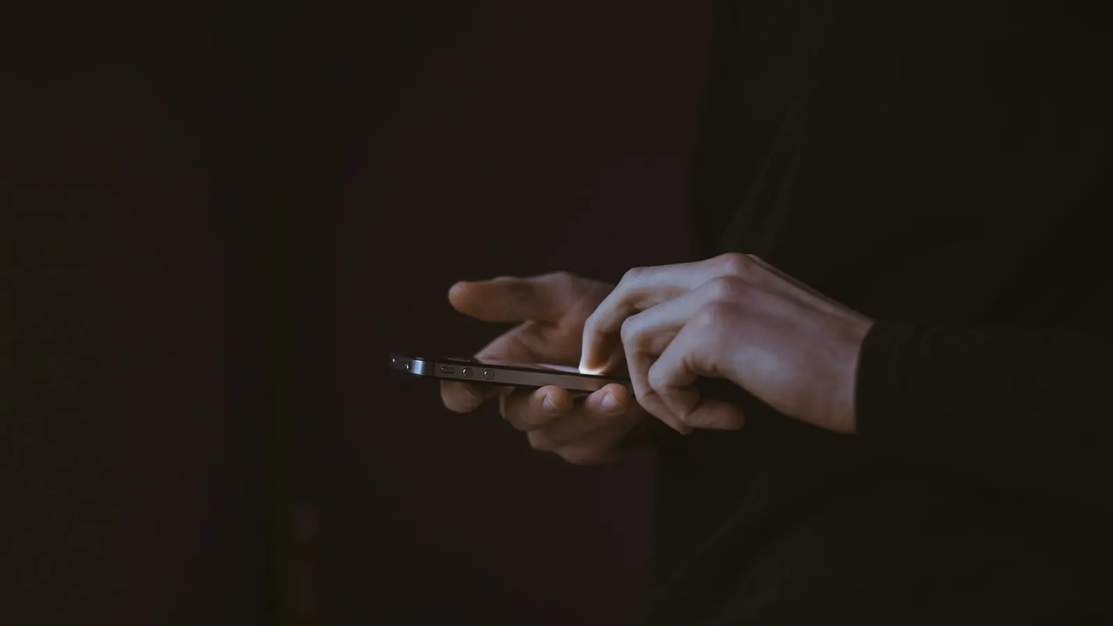 A person in the dark scrolling a smartphone